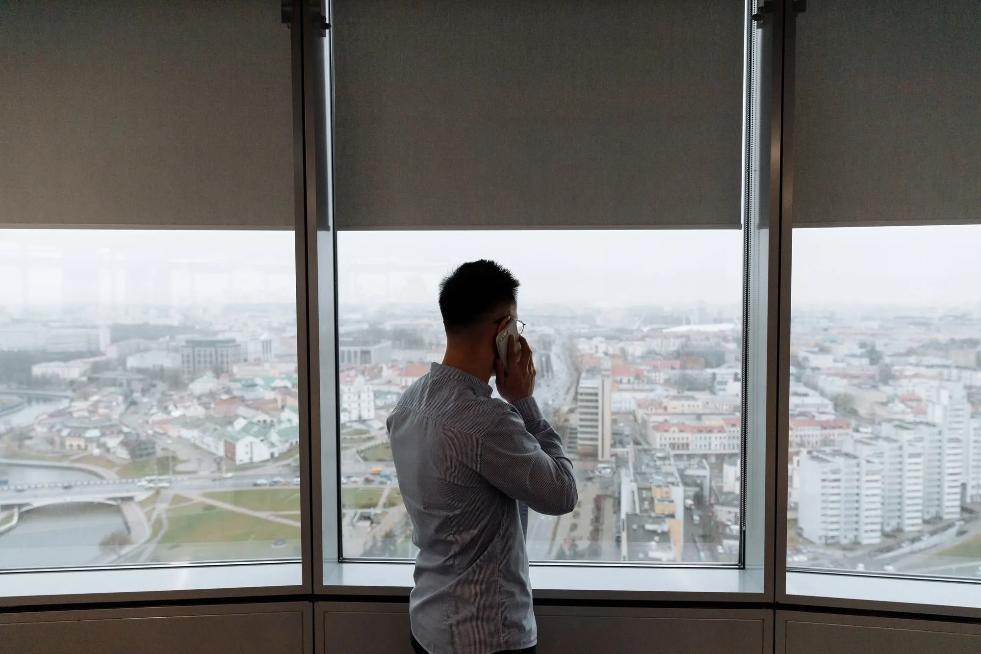 Ein Mann telefoniert vor einem Fenster mit Blick über die Stadt
