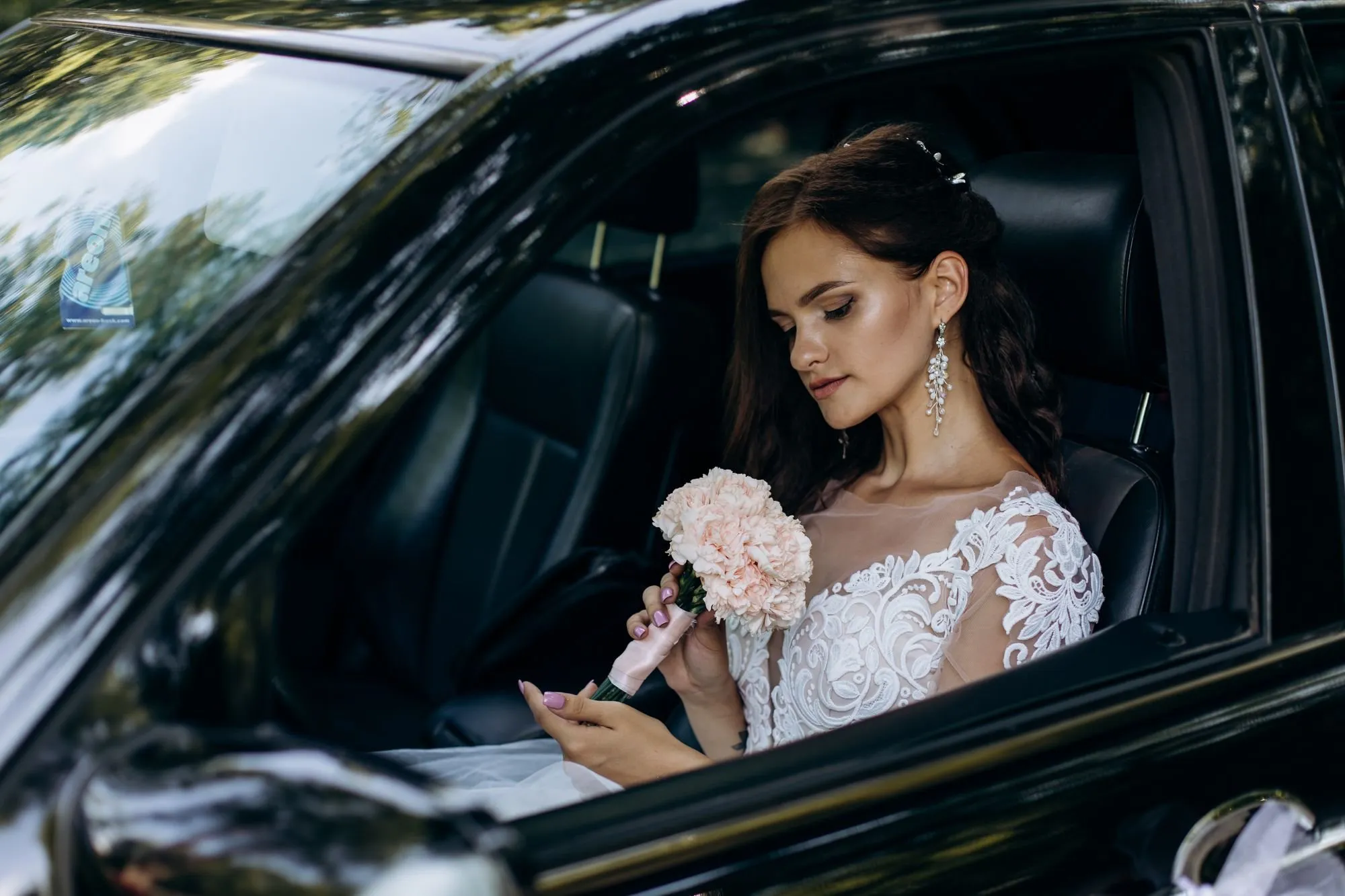 Eine Braut im Brautkleid sitzt mit Blumenstrauß in einem Auto